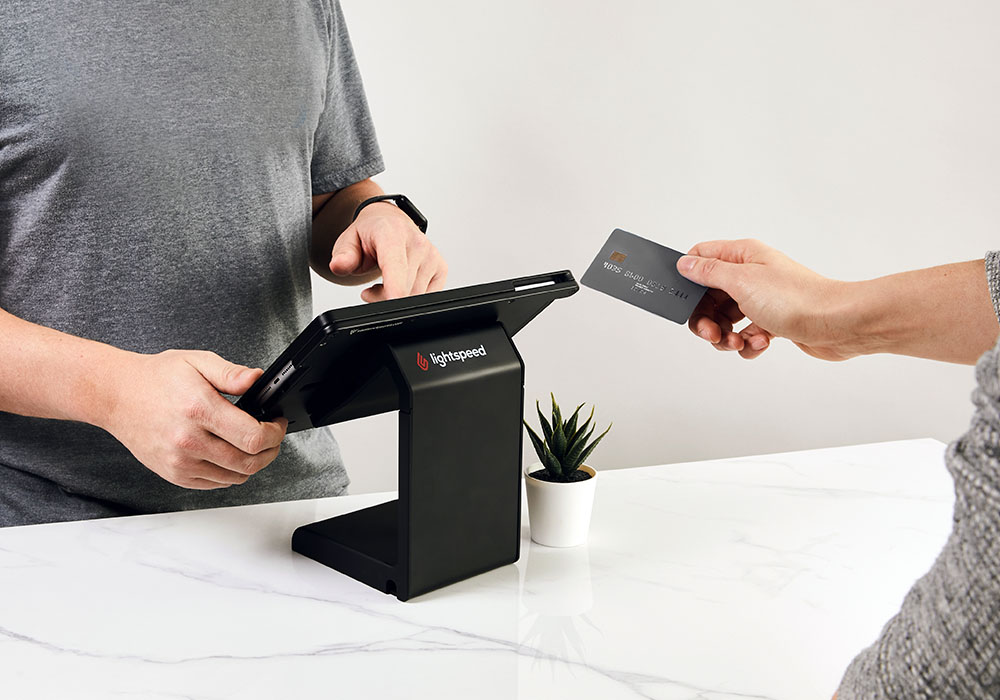 Retailer processing a payment on Lightspeed Retail, customer's hand reaches toward iPad with a card in it